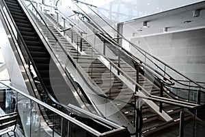 Escalators in big modern area. No people around. Grey tones interior design with shiny glass. Perspective side view. Natural