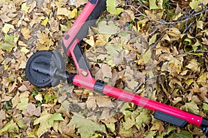 Escooter left on the ground covered with dry leaves. Red escooter side view photo