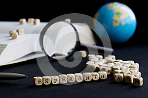 Esperanto inscription next to magnifying glass, open book, letters and small globe. Concept of learning and using the Esperanto