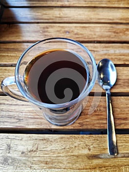 Espresso black tea coffee in a transparent glass cup with a tea spoon on a wooden table high angle shot