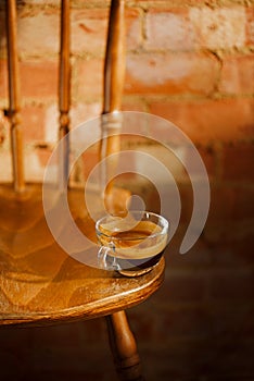 espresso coffee in clear glass cup on vintage chair with old brick wall