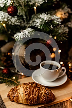 Espresso coffee, croissant near christmas tree on table. Coffee break