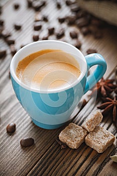 Espresso coffee cup, sugar cubes, coffee beans and spices on wooden desk.