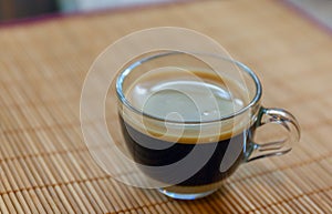 Espresso coffee with golden fine-bubbled crema seen from above in a crystal clear cup on bamboo plate holder.