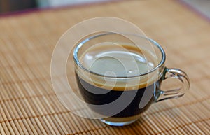 Espresso coffee with golden fine-bubbled crema seen from above in a crystal clear cup on bamboo plate holder. photo