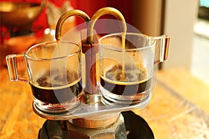 Espresso coffee trickling out from mini retro brewing pot into a pair of glass demitasse cups photo