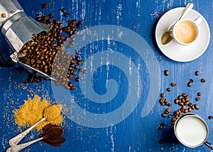 Espresso cup, cream, arabika beans in moka pot, brown sugar and ground coffee on wooden blue painted background