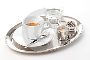 Espresso with glass of water with cream and cake on metal plate, isolated on white background, product photography of coffee