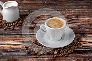 Espresso macchiato in white porcelain cup with milk and coffee beans on wooden table