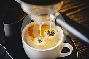 Espresso pours from the coffee machine into a white Cup forming golden foam