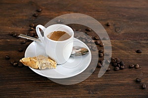 Espresso in a small white coffee cup, spoon and roasted beans on a dark rustic wooden table, copy space, selected focus