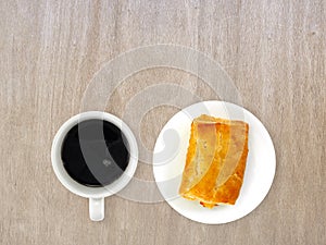 espresso in white ceramic coffee cup and chicken pie on white pottery plate on brown wooden table