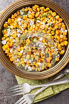 Esquites Mexican Street Food with Corn, Lime, Onion, Herbs, Cotija Cheese and Chili close-up on the plate on the table. Vertical