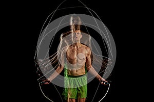 Essence of sport and athleticism. Muscular man in motion, training, doping cardio, jumping rope against black background