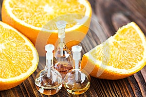 Essential aroma oil in glass bottle with fresh, juicy, ripe, orange fruit on wooden background. Beauty treatment. Spa concept. Sel