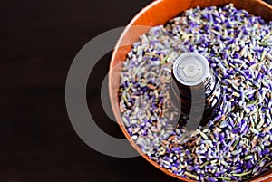 Essential lavender oil in a wooden bowl with dried lavender buds.
