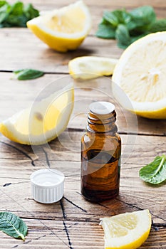 Essential lemon oil in bottle, fresh fruit slices on wooden background. Natural fragrances