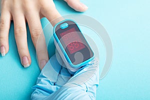 An essential medical device for hypoxia. A hand in a medical glove holds a pulse oximeter on a blue background
