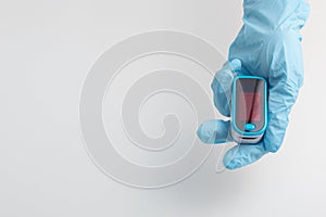 An essential medical device for hypoxia. Hand in a medical glove holds a pulse oximeter on a white background