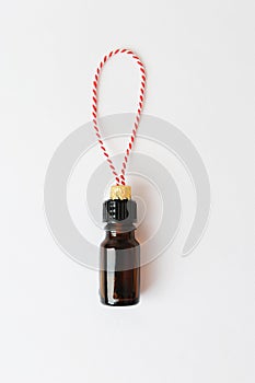 Essential oil bottle as a Christmas tree toy on red-white string on a white background. Beauty cosmetic New Year concept