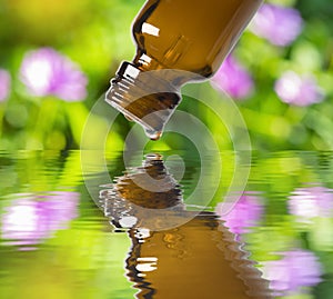 Essential oil bottle close up with a drop of oil falling into the water with reflection.