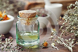 Essential oil bottle, mortars of dry medicinal herbs and old book on background