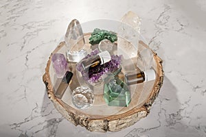 Essential oil bottles, beautiful crystals and gemstones on wooden log slice on a marble background