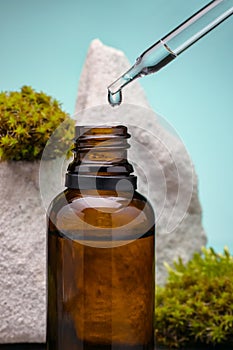 Essential oil in brown glass bottle among the moss and pipette with drop against green background