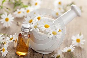 Essential oil and camomile flowers in mortar