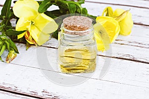 Essential oil of evening primrose in glass bottle, yellow flowers on white table, alternative medicine