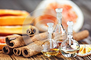 Essential oil in glass bottle with cinnamon sticks and dried red circle slices of citrus fruits orange and lemons on wooden backgr