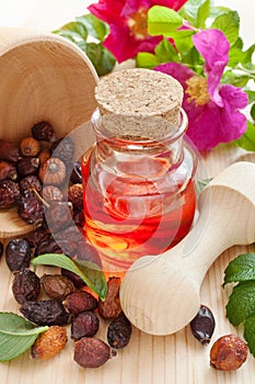 Essential oil in glass bottle, dried rose-hip berries and rose h