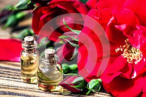Essential oil in glass bottle with red rose flowers and petals on wooden background. Beauty treatment. Spa and aromatherapy concep