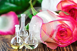 Essential oil in glass bottle with rose flowers on wooden background. Small bottles of perfume. Beauty treatment. Spa concept. Sel