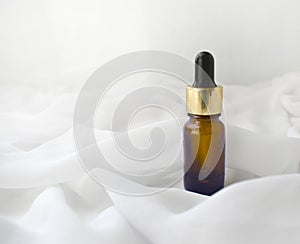 Essential oil or perfume bottle dropper on silk waved background. Minimalist luxury spa aromatherapy or bodycare concept.