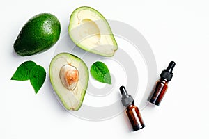 Essential oils bottles and avocado with green leaves on white background. Flat lay, top view. Aromatherapy massage oil, avocado