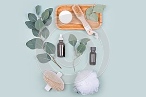 Essential oils, facial creme container and massage brushes with natural eucalyptus leaves on green background. Beauty products,