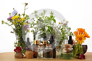 Essential oils with herbs and flowers on wooden table