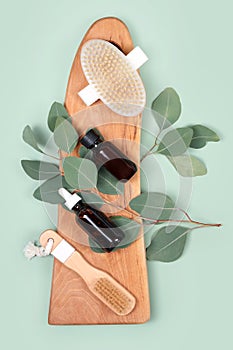 Essential oils and massage brushes with natural eucalyptus leaves on green background. Beauty products, massage tools, facial skin