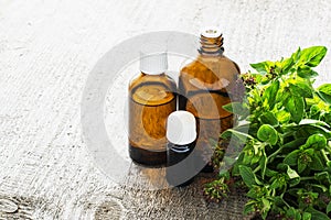 Essential oregano oil for aromatherapy in a dark glass containers on wooden background with fresh oregano. Selective