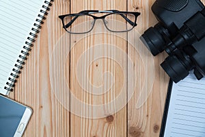 Essential vacation items, sneakers, glasses, smart phone, binocular, notebook and pen on wooden floor, top view with copy