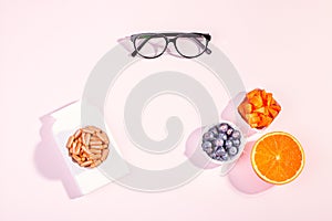 Essential vitamins and supplements to keep eyes healthy on pink background. Eyeglasses, vitamin pills, food containing vitamins
