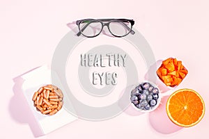 Essential vitamins and supplements to keep eyes healthy on pink background. Eyeglasses, vitamin pills, food containing vitamins