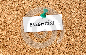 Essential. Word written on a piece of paper, cork board background