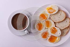 Esspresso coffee and soft boiled egg halves on the white plate and bread slices