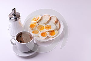 Esspresso coffee and soft boiled egg halves on the white plate and bread slices