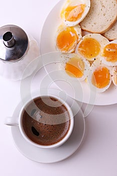 Esspresso coffee and soft boiled egg halves on the white plate and bread slices