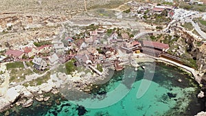 Establishing arc aerial shot of turquoise sea bathing a Mediterranean shore on Anchor Bay, Popeye Village, Malta