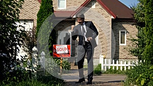 Estate agent in business suit showing yes gesture standing in front of sold home