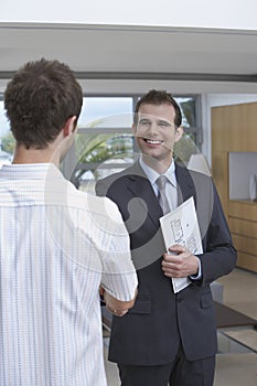 Estate Agent Shaking Hands With Customer Indoors